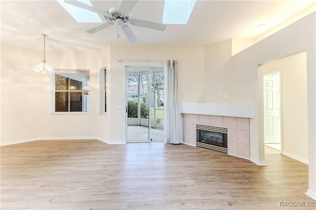 unfurnished living room with ceiling fan, a skylight, a tile fireplace, and light wood-type flooring