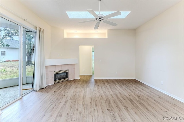 unfurnished living room featuring ceiling fan, light wood-type flooring, a fireplace, and a skylight