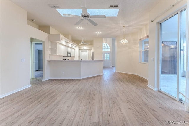 unfurnished living room with ceiling fan with notable chandelier and light hardwood / wood-style floors