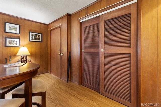 hallway featuring a textured ceiling, light wood-type flooring, and wood walls