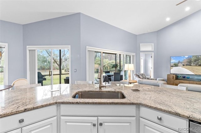 kitchen with white cabinetry, sink, light stone countertops, and vaulted ceiling