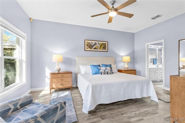 bedroom with ceiling fan, light hardwood / wood-style flooring, multiple windows, and ensuite bath