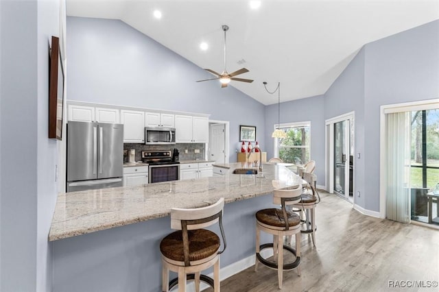 kitchen featuring high vaulted ceiling, backsplash, a breakfast bar area, white cabinets, and appliances with stainless steel finishes