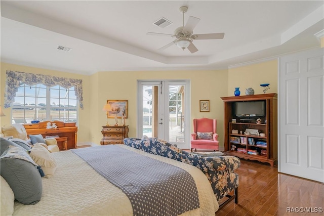 bedroom with wood-type flooring, a raised ceiling, multiple windows, and access to outside