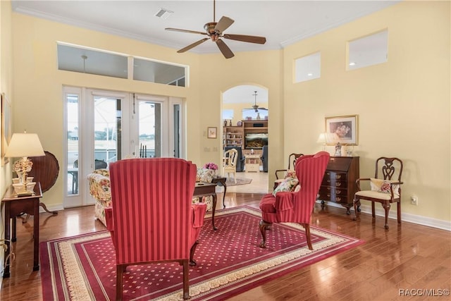 living area with crown molding, ceiling fan, a towering ceiling, and hardwood / wood-style flooring