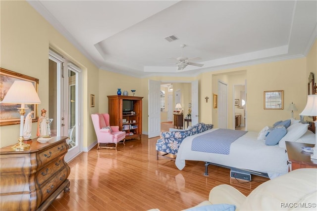 bedroom featuring connected bathroom, wood-type flooring, ornamental molding, a tray ceiling, and ceiling fan