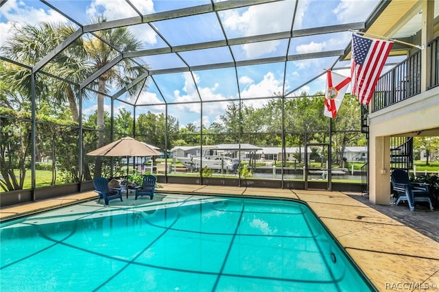 view of swimming pool featuring glass enclosure, a water view, and a patio