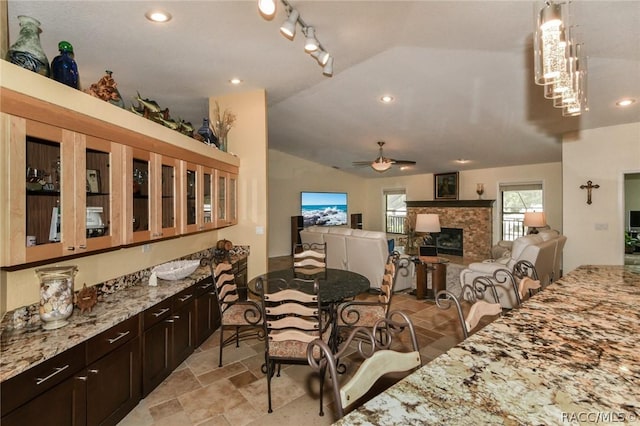 dining area featuring ceiling fan, a fireplace, track lighting, and vaulted ceiling