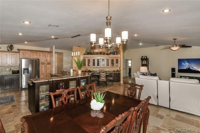 dining space with a textured ceiling, lofted ceiling, ceiling fan with notable chandelier, and sink