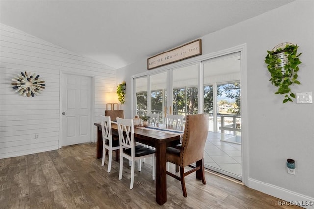 dining room with hardwood / wood-style flooring, vaulted ceiling, and wooden walls