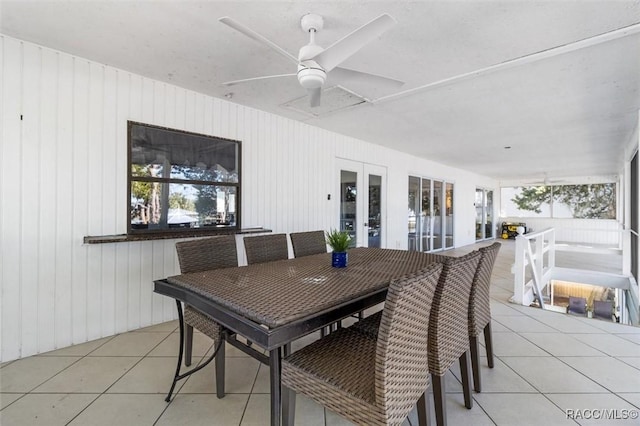 dining room with ceiling fan, light tile patterned floors, and wood walls