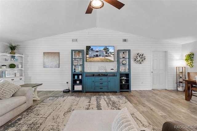 living room with light wood-type flooring, vaulted ceiling, ceiling fan, and wooden walls