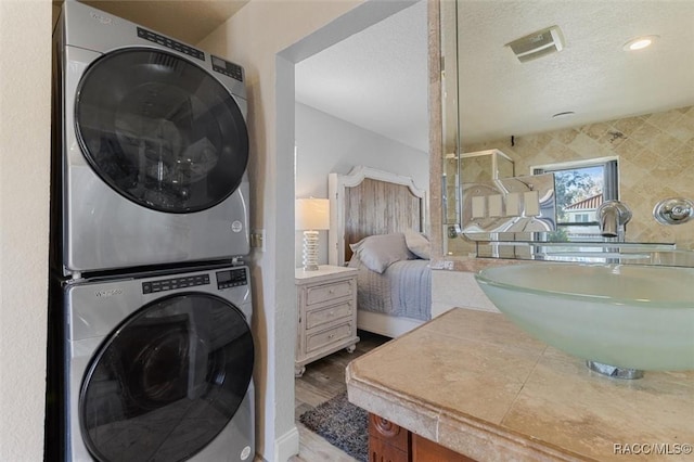 laundry area with a textured ceiling, light hardwood / wood-style flooring, stacked washer / dryer, and sink