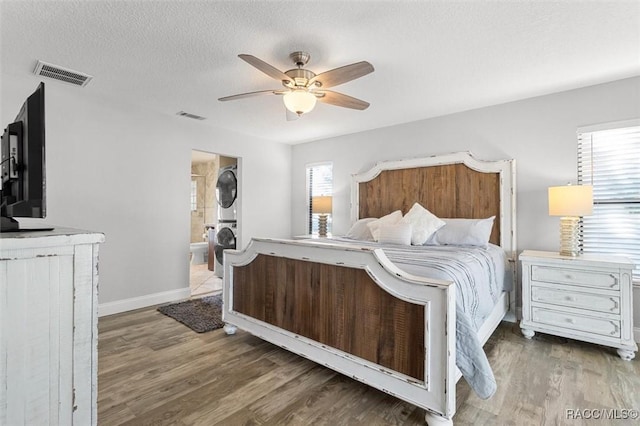 bedroom with ceiling fan, wood-type flooring, a textured ceiling, and stacked washer and clothes dryer