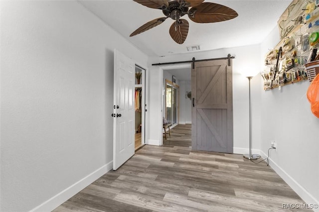 unfurnished room featuring a barn door, light hardwood / wood-style flooring, and ceiling fan