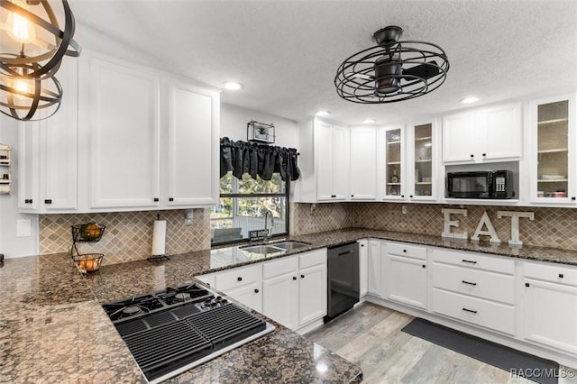 kitchen with dark stone counters, sink, black appliances, white cabinets, and hanging light fixtures