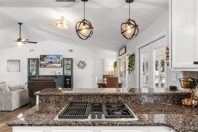 kitchen featuring pendant lighting, vaulted ceiling, dark stone countertops, white cabinetry, and stainless steel gas cooktop