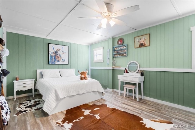 bedroom featuring hardwood / wood-style flooring, ceiling fan, and wood walls