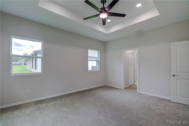 unfurnished bedroom featuring ceiling fan, light carpet, a tray ceiling, and multiple windows