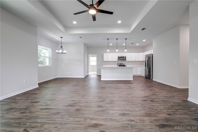 unfurnished living room with ceiling fan with notable chandelier, dark hardwood / wood-style flooring, and a tray ceiling