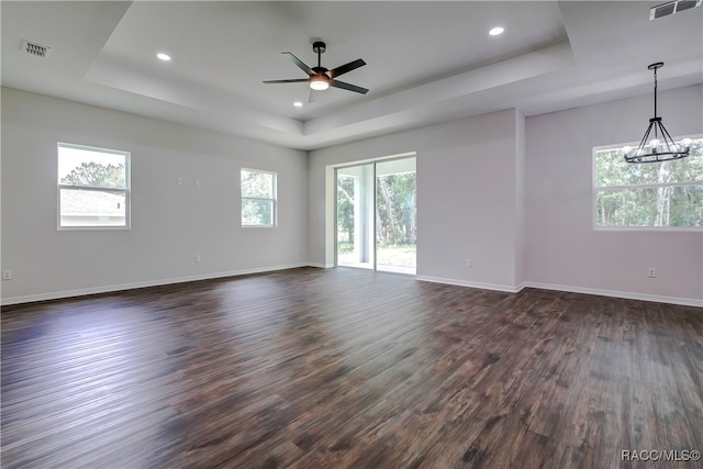 unfurnished room with a raised ceiling, ceiling fan with notable chandelier, dark hardwood / wood-style flooring, and a wealth of natural light