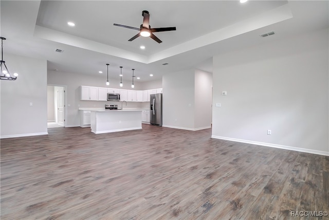 unfurnished living room featuring hardwood / wood-style floors, ceiling fan with notable chandelier, and a tray ceiling