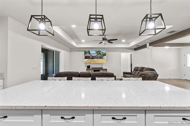 kitchen with light stone counters, ceiling fan, white cabinetry, visible vents, and open floor plan