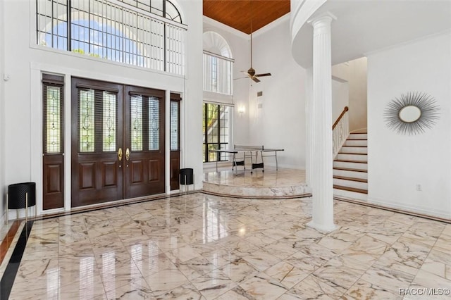 foyer featuring decorative columns, marble finish floor, ornamental molding, and stairs