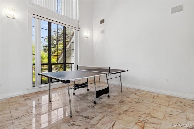 rec room with visible vents, marble finish floor, a high ceiling, and baseboards