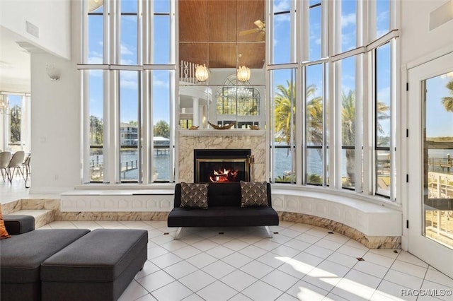 tiled living area with a high ceiling, a healthy amount of sunlight, visible vents, and a high end fireplace