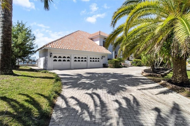 view of property exterior featuring a tiled roof, stucco siding, a lawn, a garage, and driveway