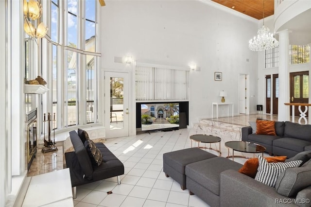 tiled living room featuring a high end fireplace, decorative columns, an inviting chandelier, and a towering ceiling