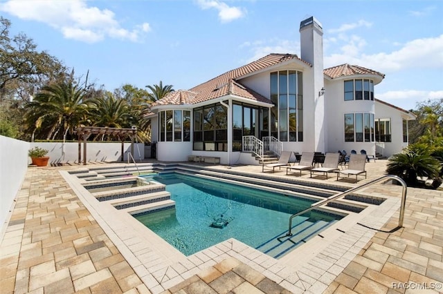 rear view of house with stucco siding, a tile roof, a sunroom, a chimney, and a patio area