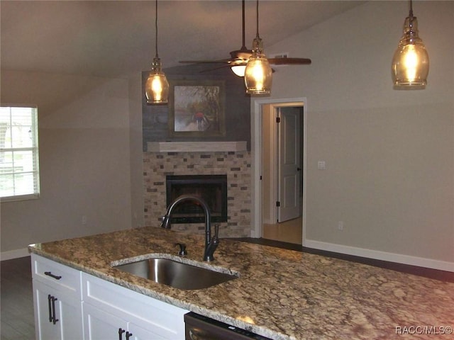 kitchen featuring sink, white cabinetry, hanging light fixtures, a fireplace, and light stone countertops