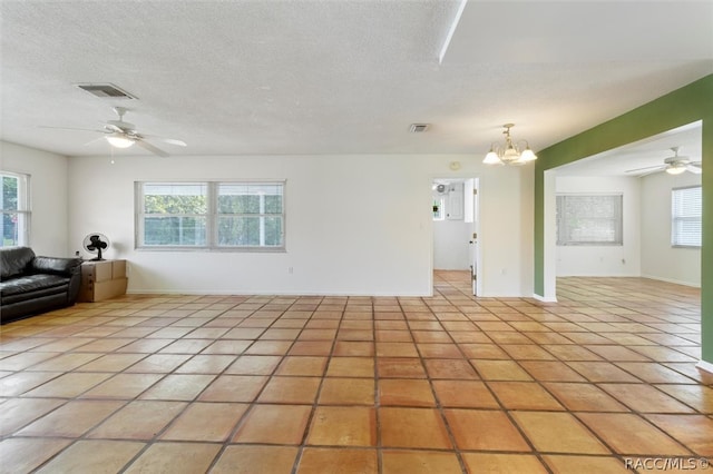 unfurnished living room featuring ceiling fan with notable chandelier, light tile patterned floors, and a textured ceiling