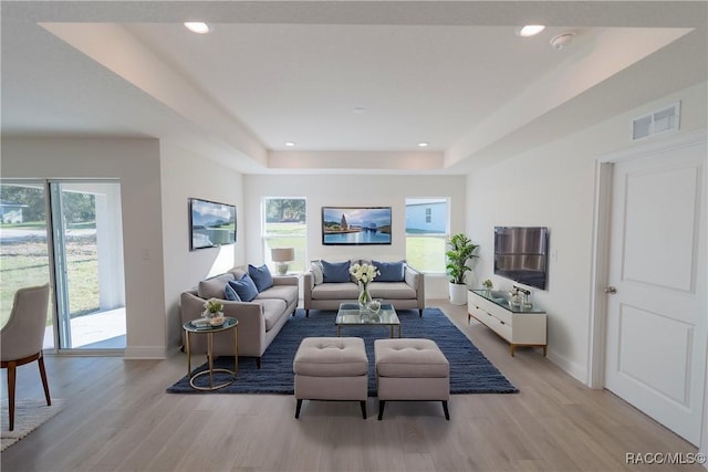 living room with light wood-type flooring, a tray ceiling, and plenty of natural light