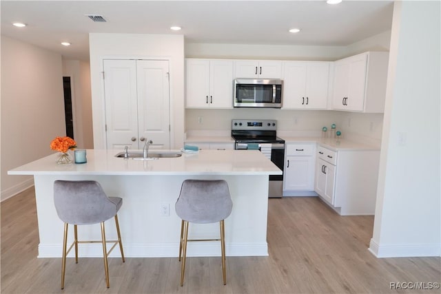 kitchen with sink, appliances with stainless steel finishes, a kitchen breakfast bar, an island with sink, and white cabinets