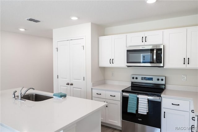 kitchen with white cabinets, appliances with stainless steel finishes, a kitchen island with sink, and sink