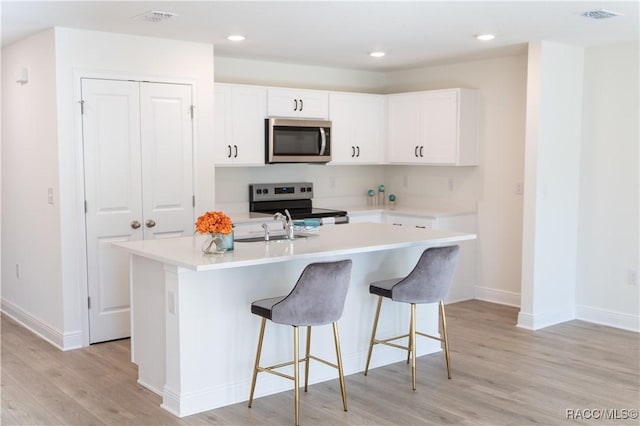 kitchen featuring appliances with stainless steel finishes, white cabinetry, sink, a kitchen island with sink, and light hardwood / wood-style floors