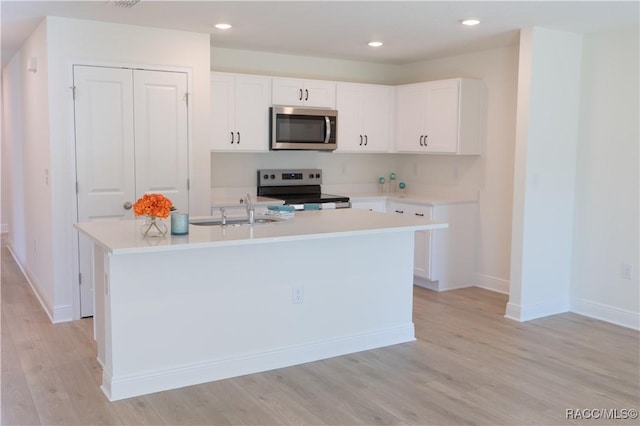 kitchen with stainless steel appliances, white cabinetry, sink, and a center island with sink