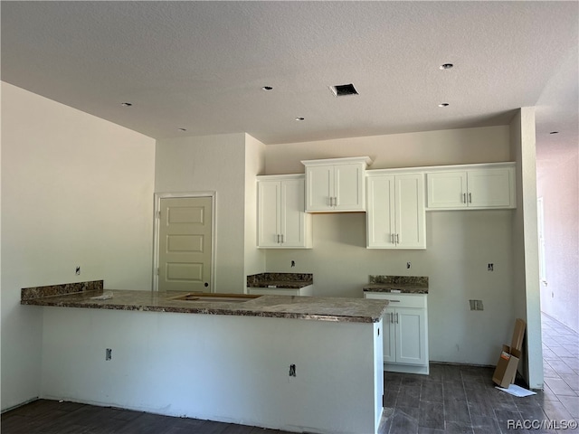 kitchen featuring kitchen peninsula, white cabinetry, dark stone countertops, and a textured ceiling