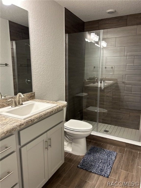 bathroom with vanity, toilet, a shower with shower door, and a textured ceiling