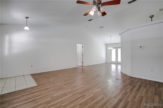 spare room with ceiling fan with notable chandelier, light hardwood / wood-style floors, and lofted ceiling