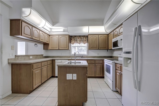 kitchen featuring white appliances, a raised ceiling, sink, light tile patterned floors, and a center island with sink