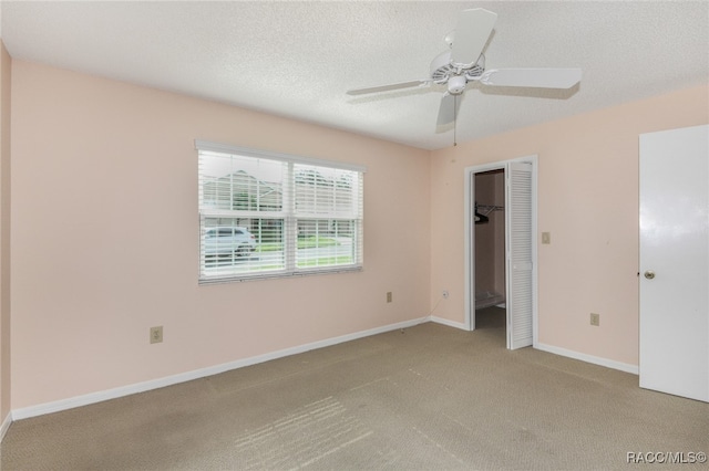 unfurnished bedroom with a textured ceiling, light colored carpet, a closet, and ceiling fan