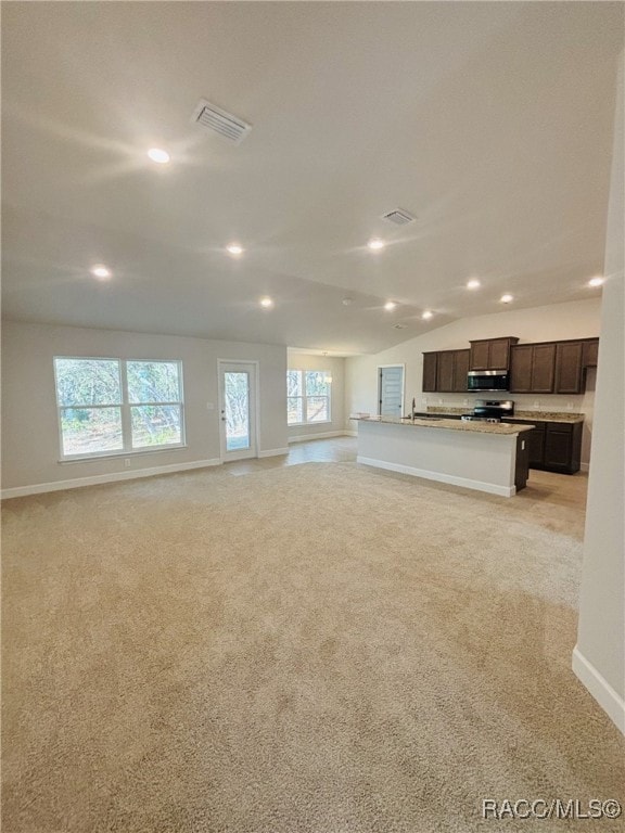 unfurnished living room featuring sink, vaulted ceiling, and light colored carpet