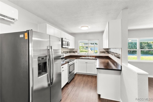 kitchen with sink, a wall mounted air conditioner, dark hardwood / wood-style floors, white cabinets, and appliances with stainless steel finishes