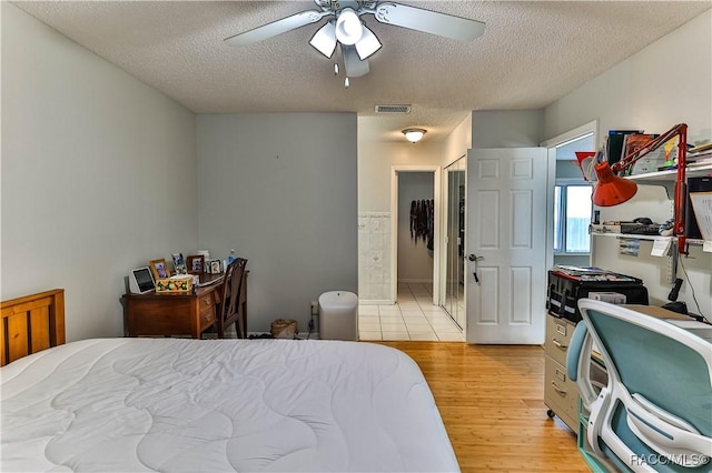 bedroom with visible vents, a ceiling fan, a textured ceiling, ensuite bath, and light wood finished floors