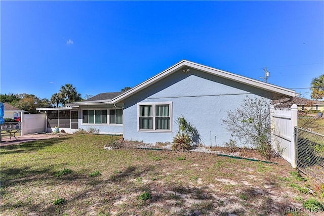 rear view of house with a yard, fence, stucco siding, and a sunroom