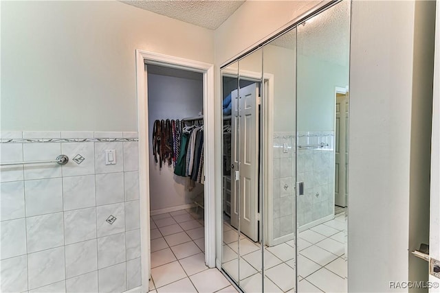 bathroom with a walk in closet, a textured ceiling, tile walls, wainscoting, and tile patterned flooring